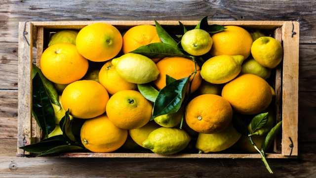 A wooden box of fresh citrus, lemons, and oranges with green leafs
